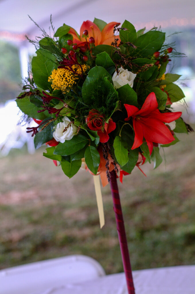 Bridal bouquet of red lilies, garden roses and yellow yarrow with a burgundy-wrapped handle.