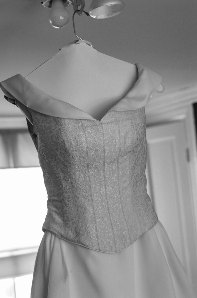 A brocade corset wedding gown on a hanger in soft window light, black and white.