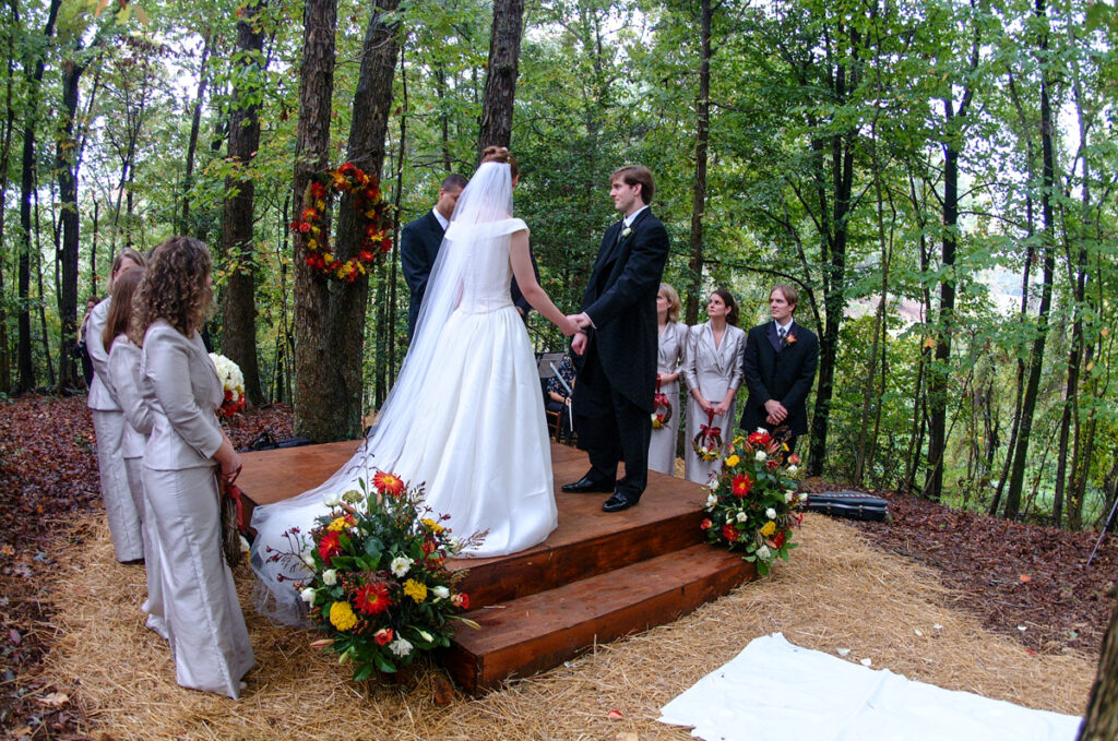 Black-and-white close-up of the couple’s hands during the ring exchange, a guest watching behind.