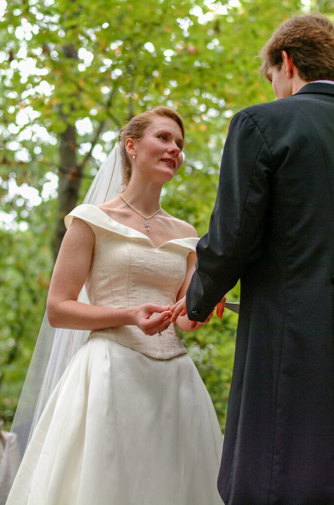 The bride tears up looking at the groom during their vows, autumn woods behind.