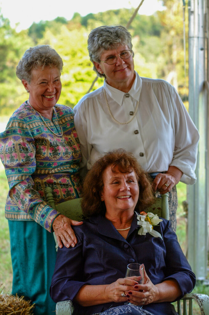 Three women at the reception, two standing behind a third seated in a chair.