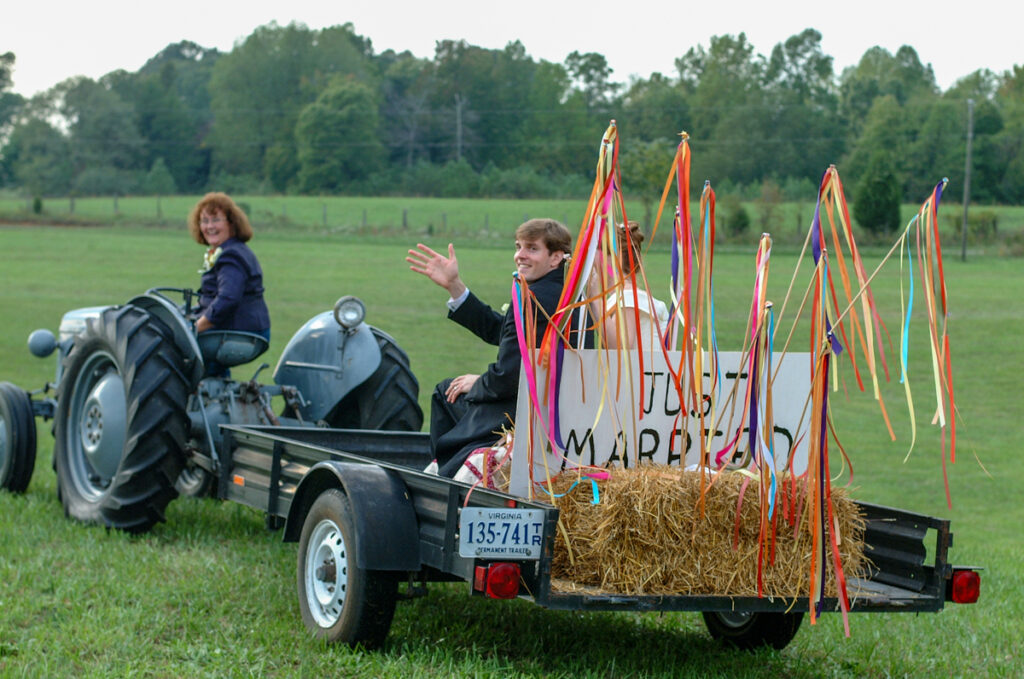 The couple leaves on a ribbon-decked hay trailer pulled by a vintage tractor across the pasture.